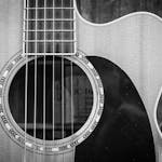 Detailed black and white photo of an acoustic guitar showcasing strings and sound hole.