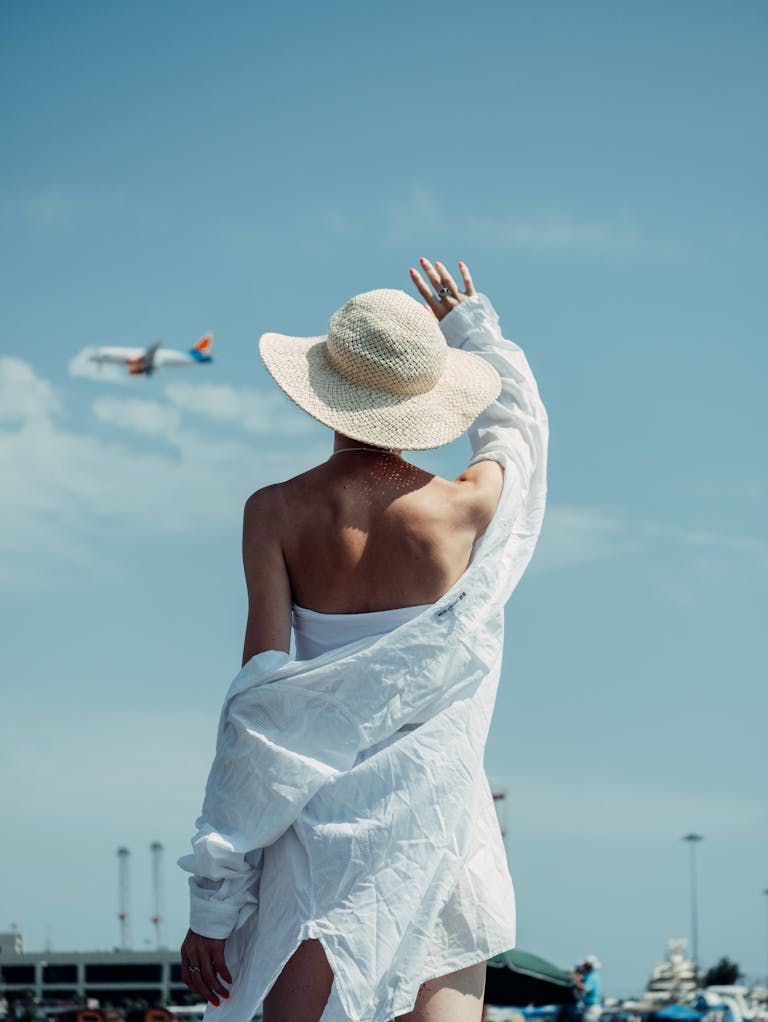 A woman in a sun hat waves at an airplane in Sochi, offering a bright summer vibe.