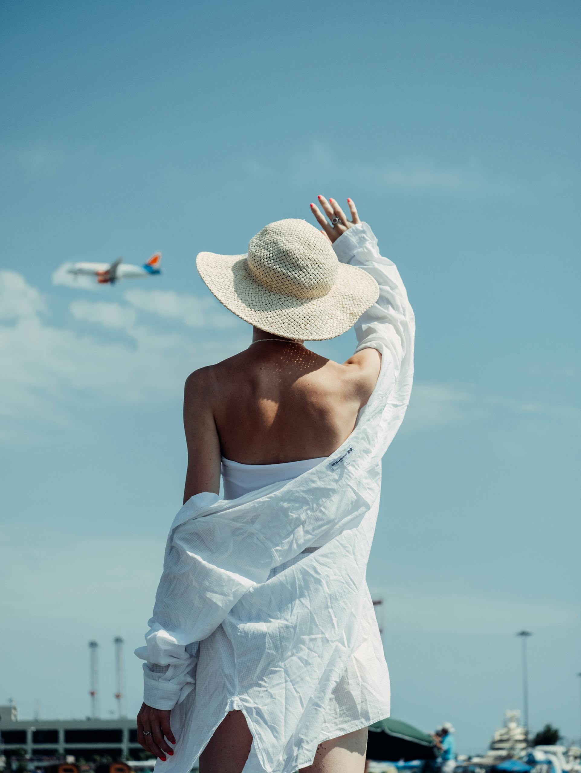A woman in a sun hat waves at an airplane in Sochi, offering a bright summer vibe.