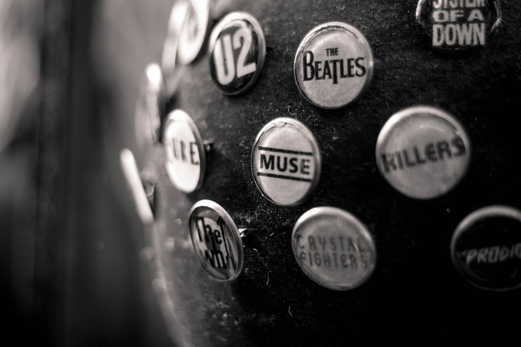 Close-up of vintage music band pins on black fabric, showcasing iconic rock band logos.