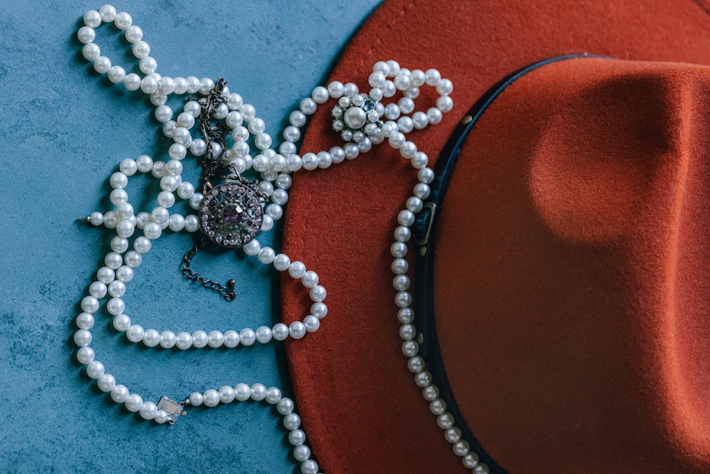 A stylish display of a red fedora and pearl jewelry against a blue background.