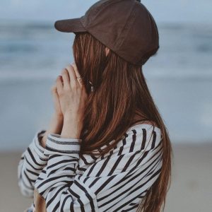 A woman in a cap stands at Sunshine Beach, capturing a peaceful seaside moment.